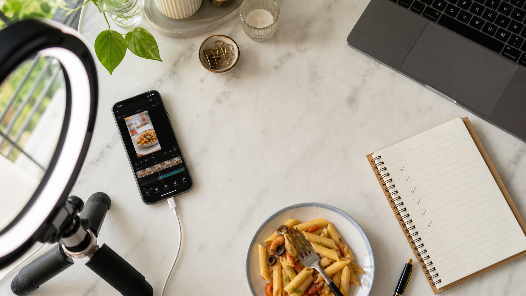 Food creator workspace with phone, pasta, notebook, and laptop